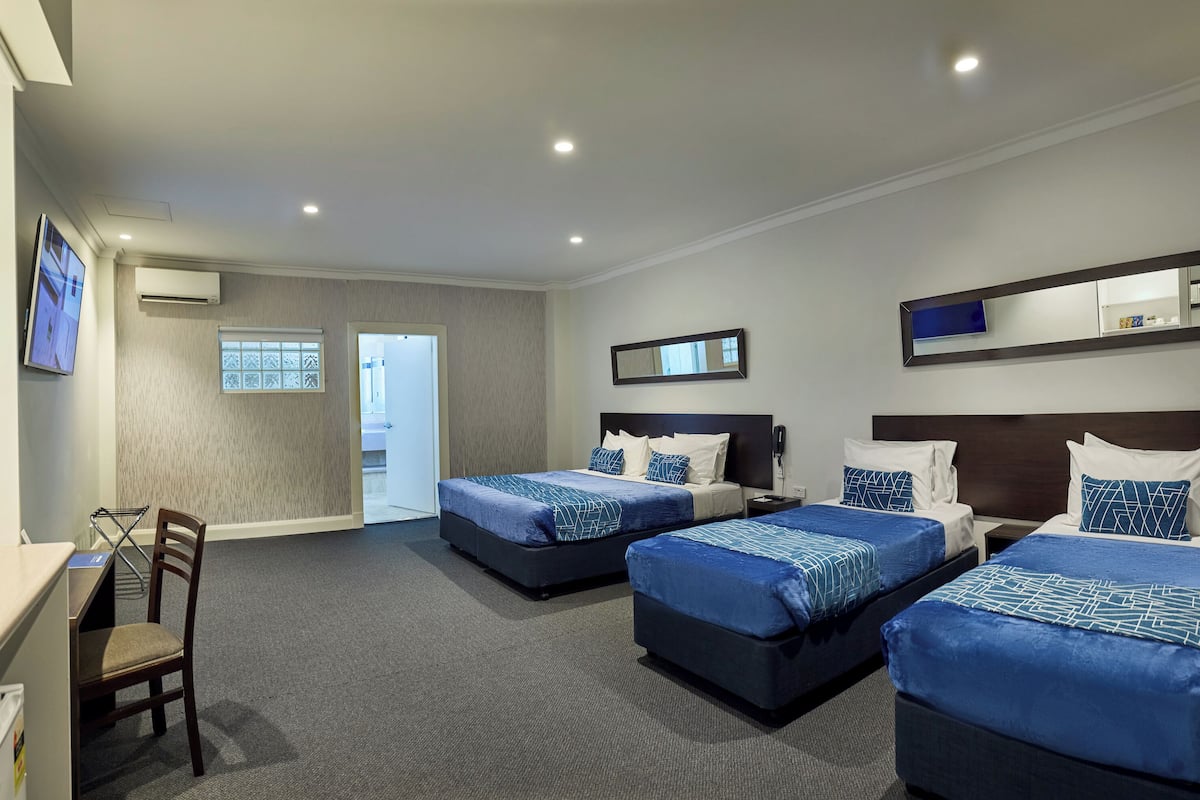 Habitación de hotel con tres camas, un escritorio y una silla.