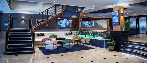 A modern lobby with a staircase, seating area, and a reception desk.