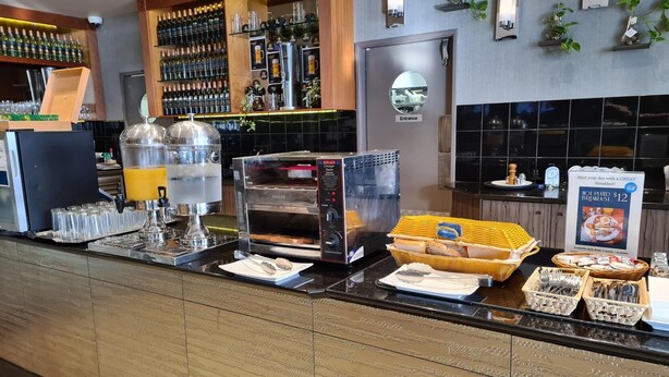 A breakfast buffet area with a self-serve coffee machine, a bread display, and a sign advertising a $12 breakfast. - Great Southern Hotel Perth (Perth)