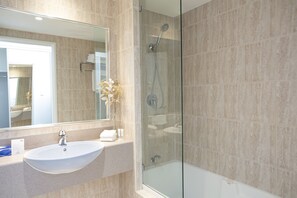 A modern bathroom with a glass-enclosed shower, a sink, and a large mirror.