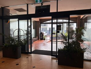 A hotel entrance with glass doors, potted plants, and a tiled floor.