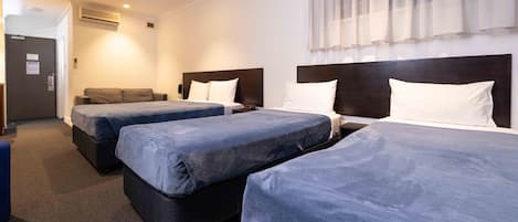 A hotel room with three beds, a sofa, and a desk.