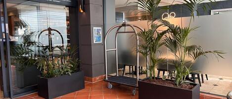 A hotel lobby with a modern design, featuring a reception desk, potted plants, and a glass entrance.