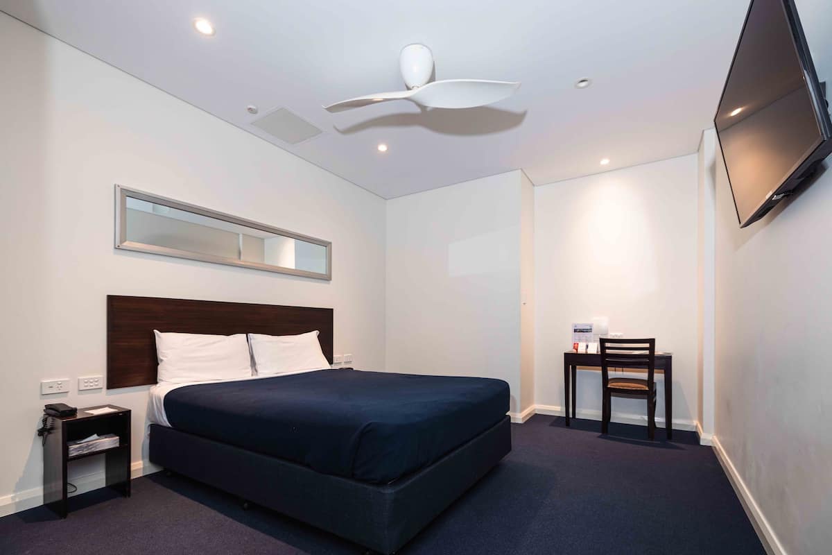 Una habitación de hotel con cama, escritorio, silla, televisor, ventilador de techo y espejo.