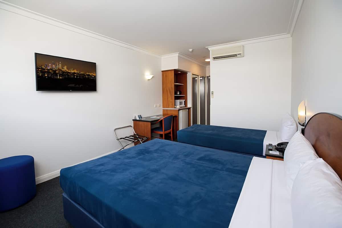 Habitación de hotel con dos camas, un escritorio, una silla, una estantería y un televisor en la pared.