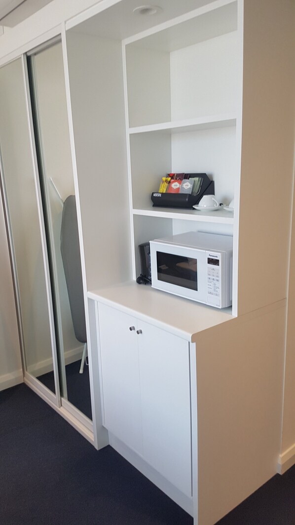 Un meuble blanc contenant un four à micro-ondes et une petite étagère avec quelques objets.
