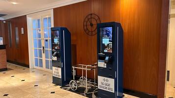 A hotel lobby with a reception desk, a self-service kiosk, and a luggage cart.