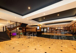 A spacious lobby with a staircase, seating area, reception desk, and a modern ceiling design.