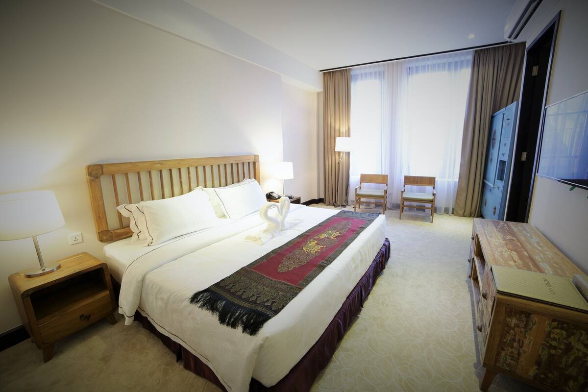 Une chambre d’hôtel avec un grand lit, une table de chevet en bois, un bureau, une chaise et un téléviseur.
