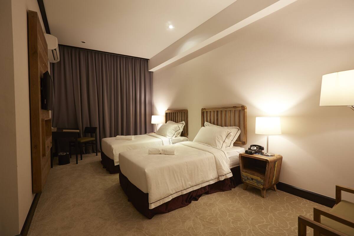 Une chambre d’hôtel avec deux lits, un bureau, une chaise et une table de chevet avec une lampe.