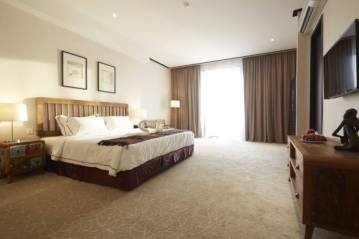 Une chambre d’hôtel avec un grand lit, une table de chevet en bois, une commode et un téléviseur à écran plat fixé au mur.