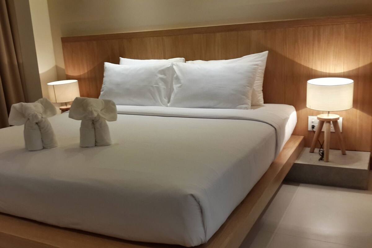 A neatly made bed with white linens, two bedside lamps, and two decorative pillows on the headboard.