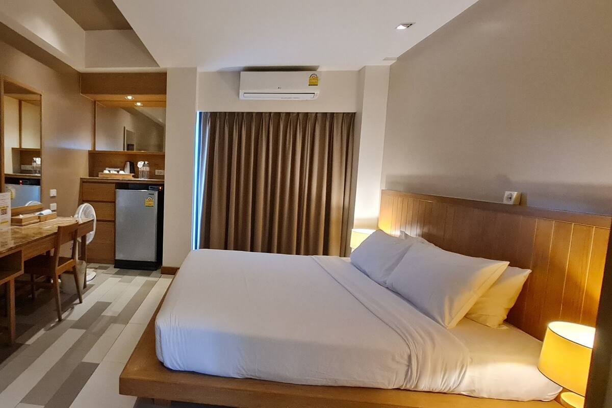 A hotel room with a bed, a desk, a chair, a television, and a kitchenette.