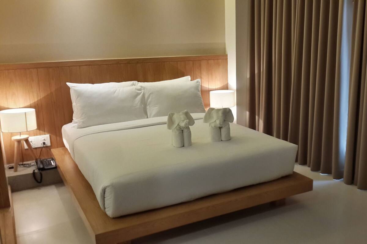 A hotel room with a bed, a bedside lamp, a telephone, and a window with curtains.