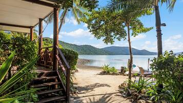 Relax on the beach with a lounge chair and table, surrounded by lush greenery and a scenic hillside backdrop.