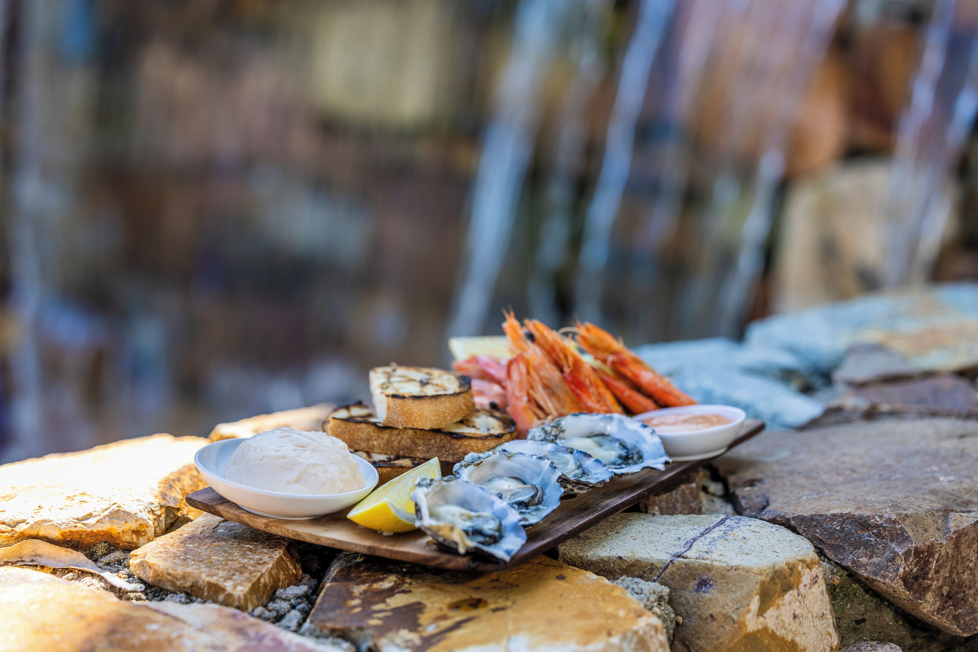Un plateau de fruits de mer comprenant des huîtres, des crevettes et du pain, le tout présenté sur une planche en bois.
