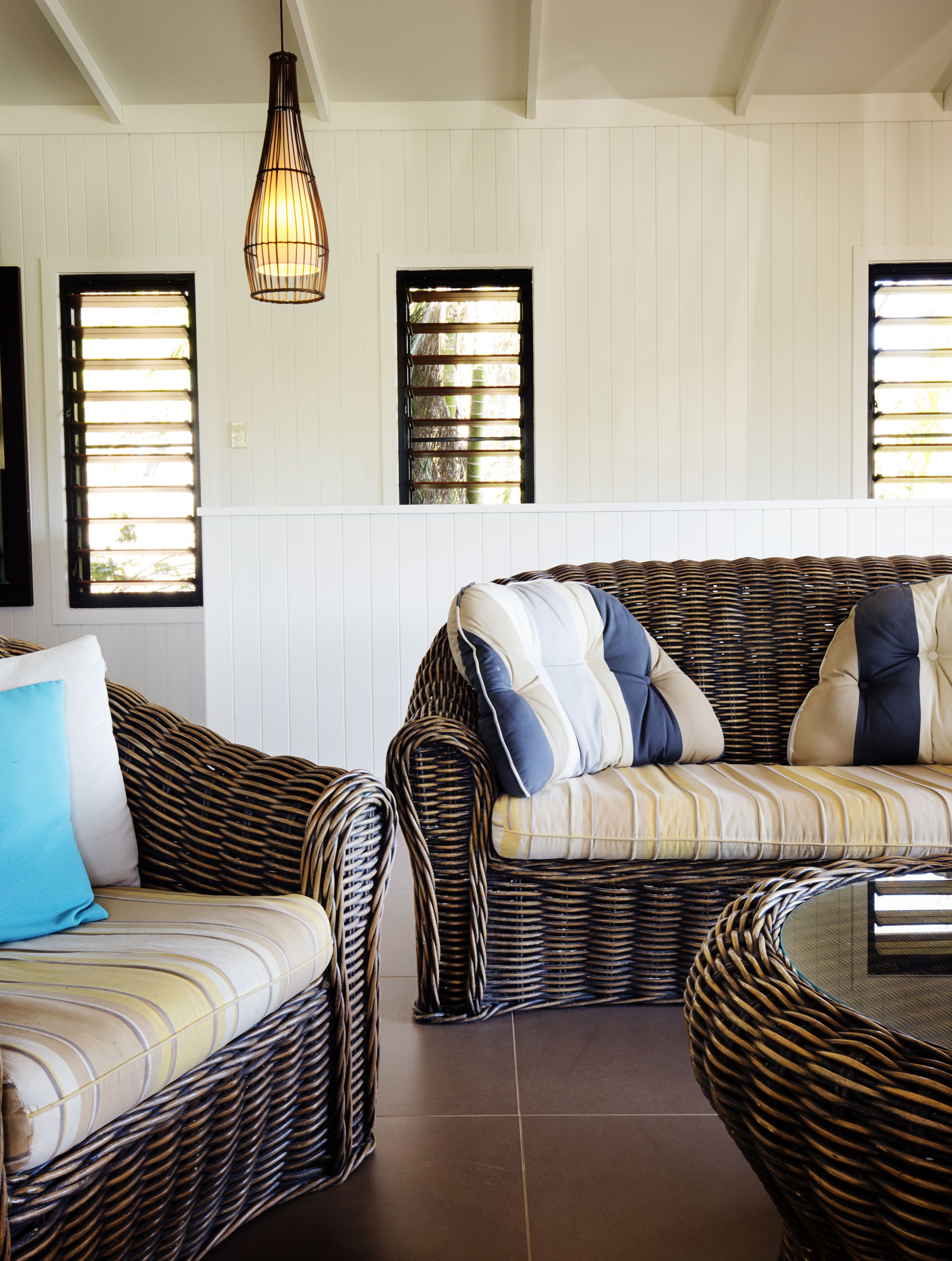 Una habitación con muebles de mimbre, incluyendo un sofá y una butaca, con una lámpara colgante arriba.