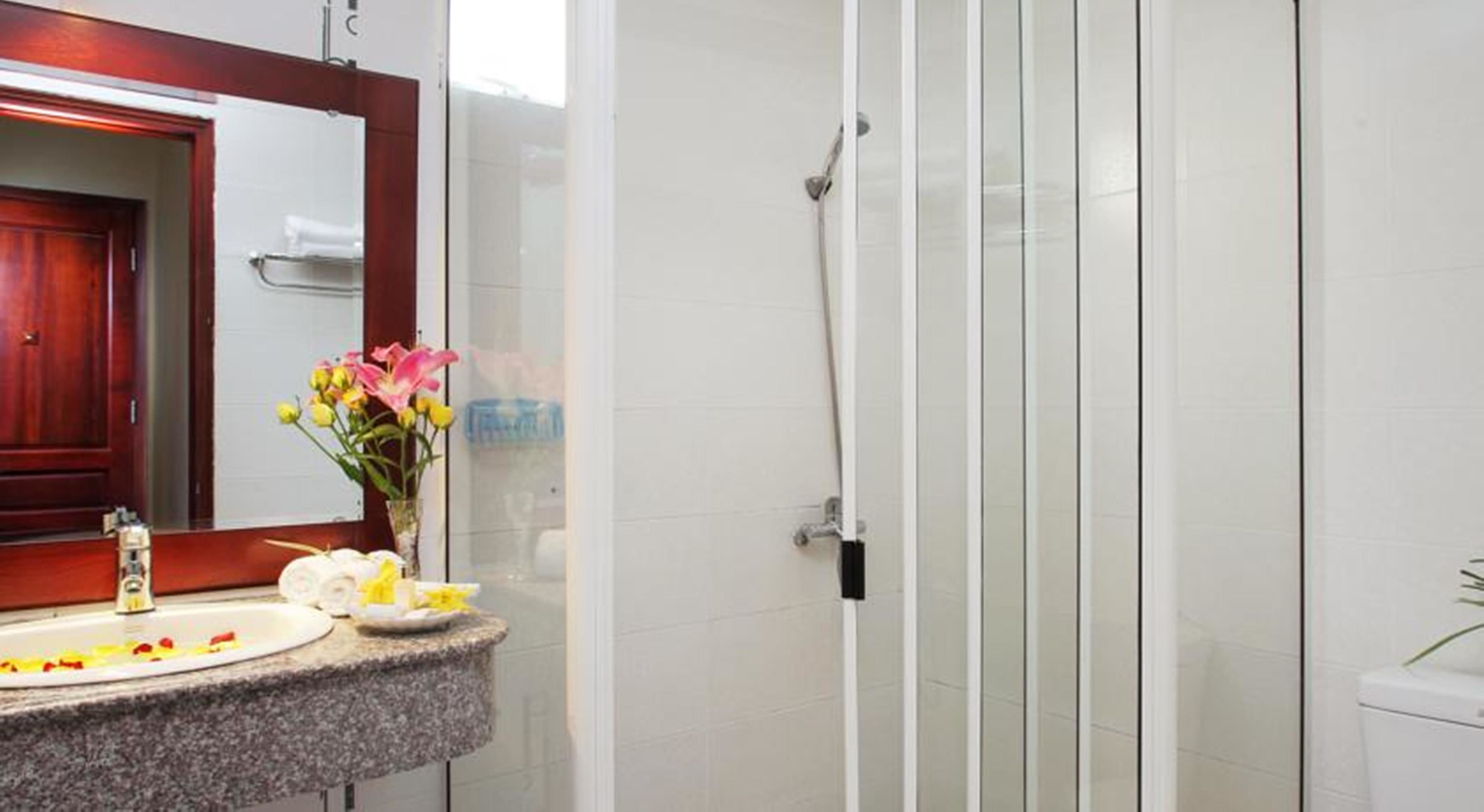 A bathroom with a shower, a sink with a mirror, and a vase with flowers.