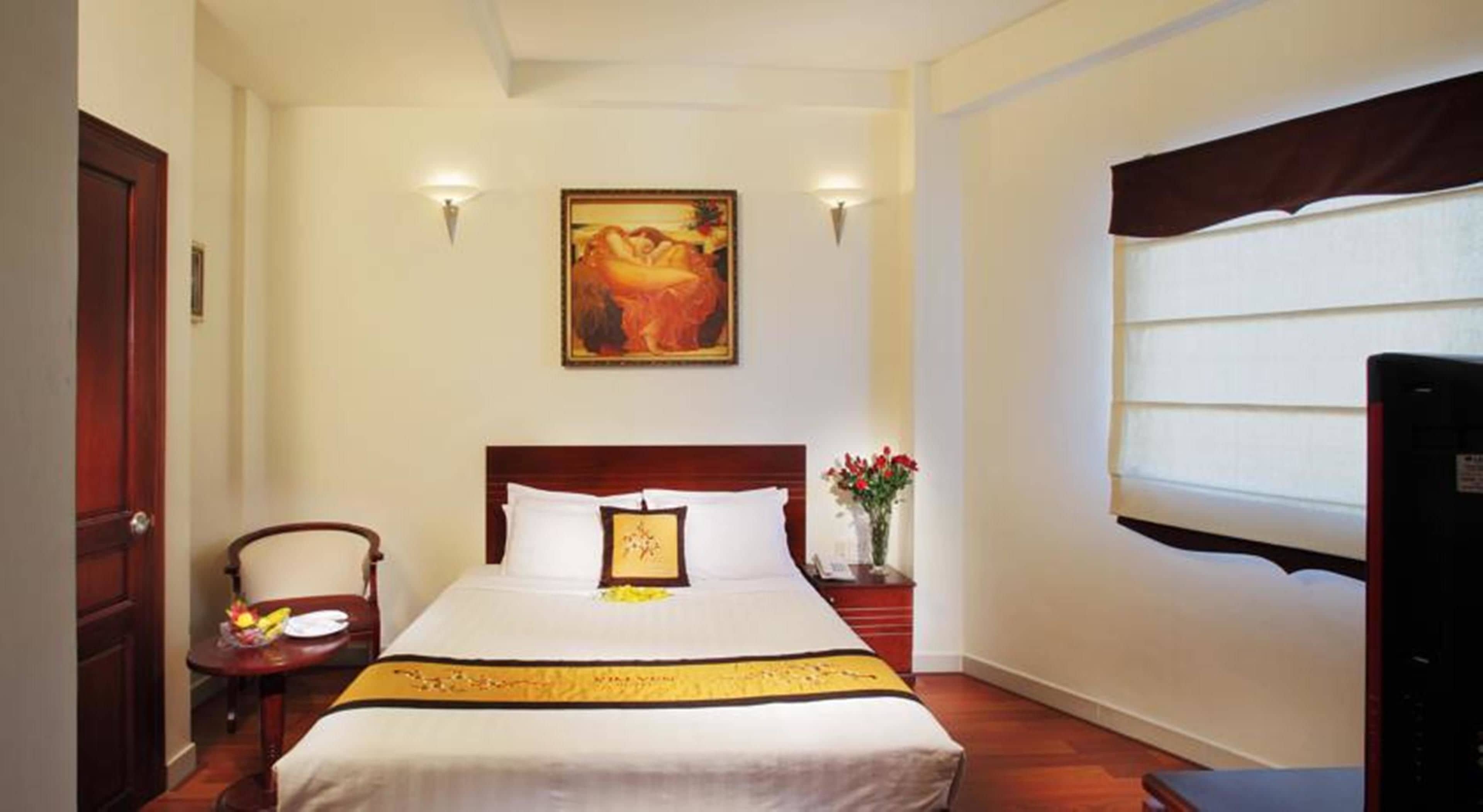 Een hotelkamer met een groot bed, een stoel, een kleine tafel, een nachtkastje, een schilderij en een raam met gordijnen.