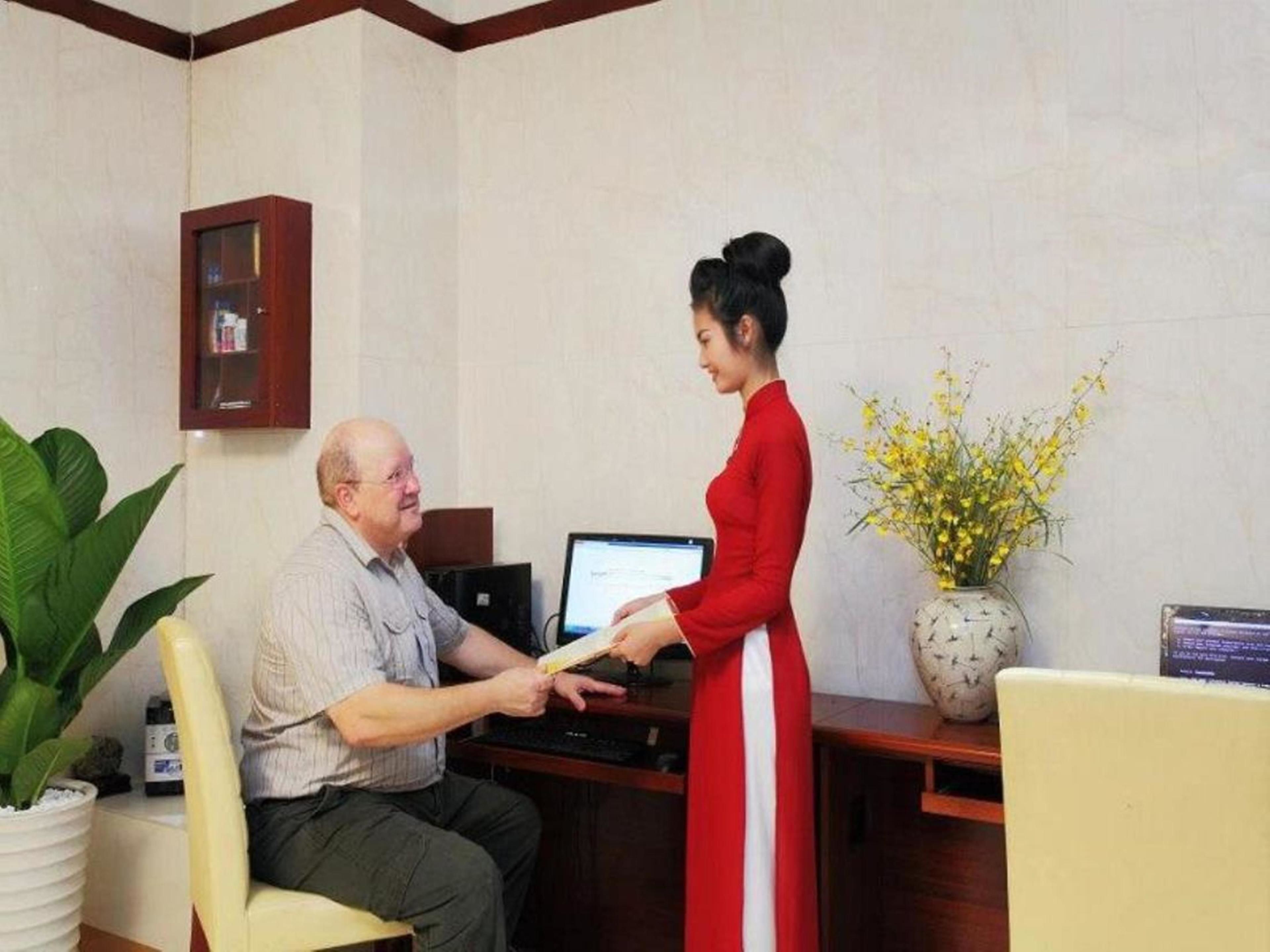 A reception area with a desk, a computer, a plant, and a vase with yellow flowers.