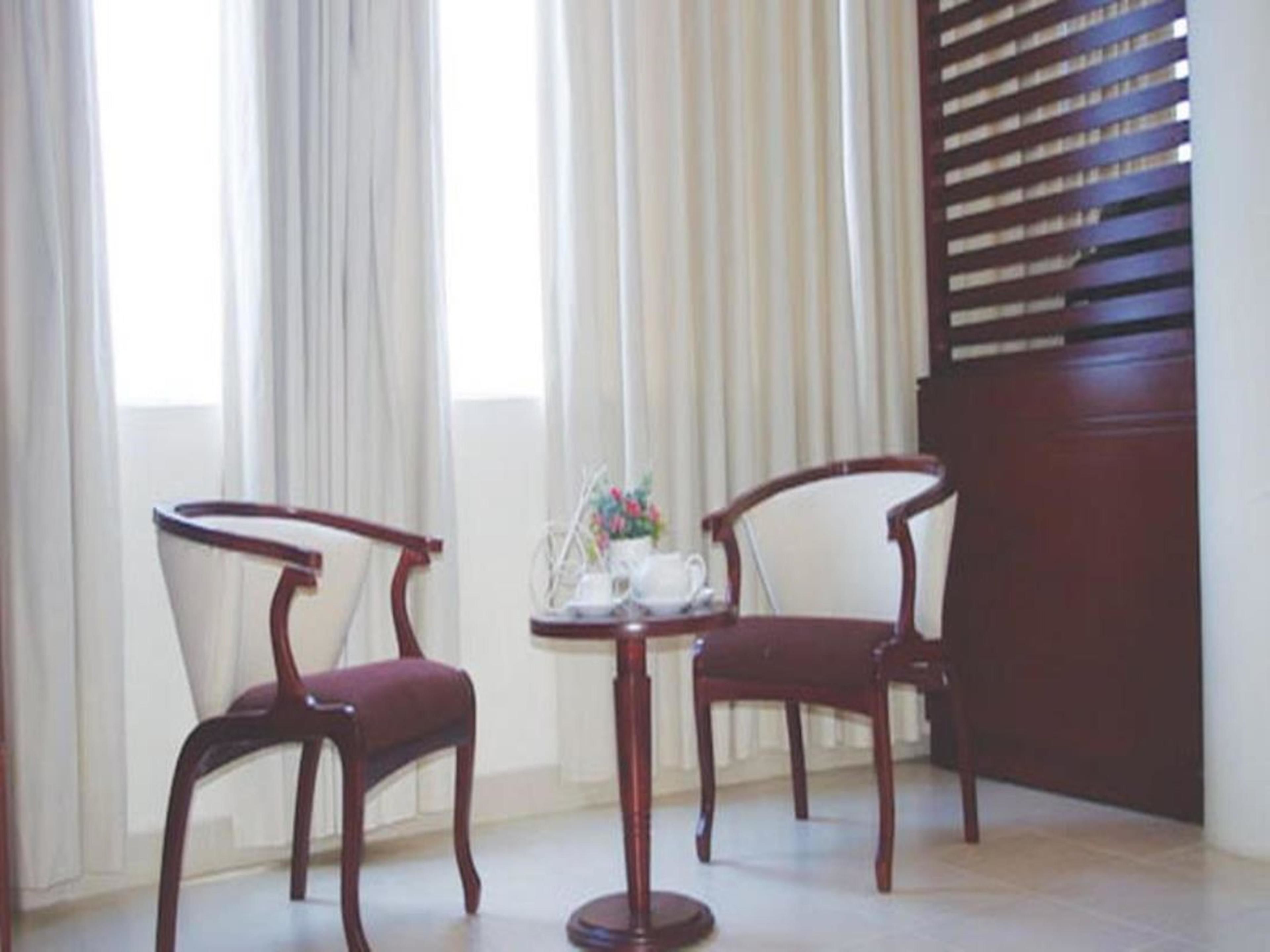 Two wooden chairs with cushioned seats and backs, positioned on a tiled floor in a room with a window and a wall with horizontal slats.