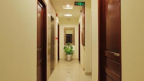 A hotel hallway with wooden doors, a potted plant, and an exit sign. - Kim Yen Hotel (Ho Chi Minh City)