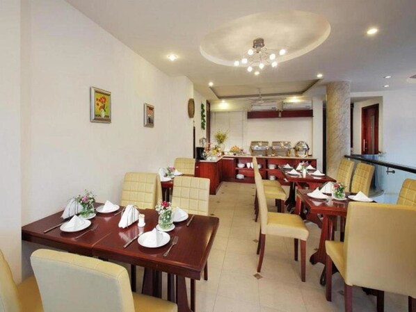 Un espace repas avec plusieurs tables et chaises, une cuisine à l’arrière-plan et un luminaire au plafond.
