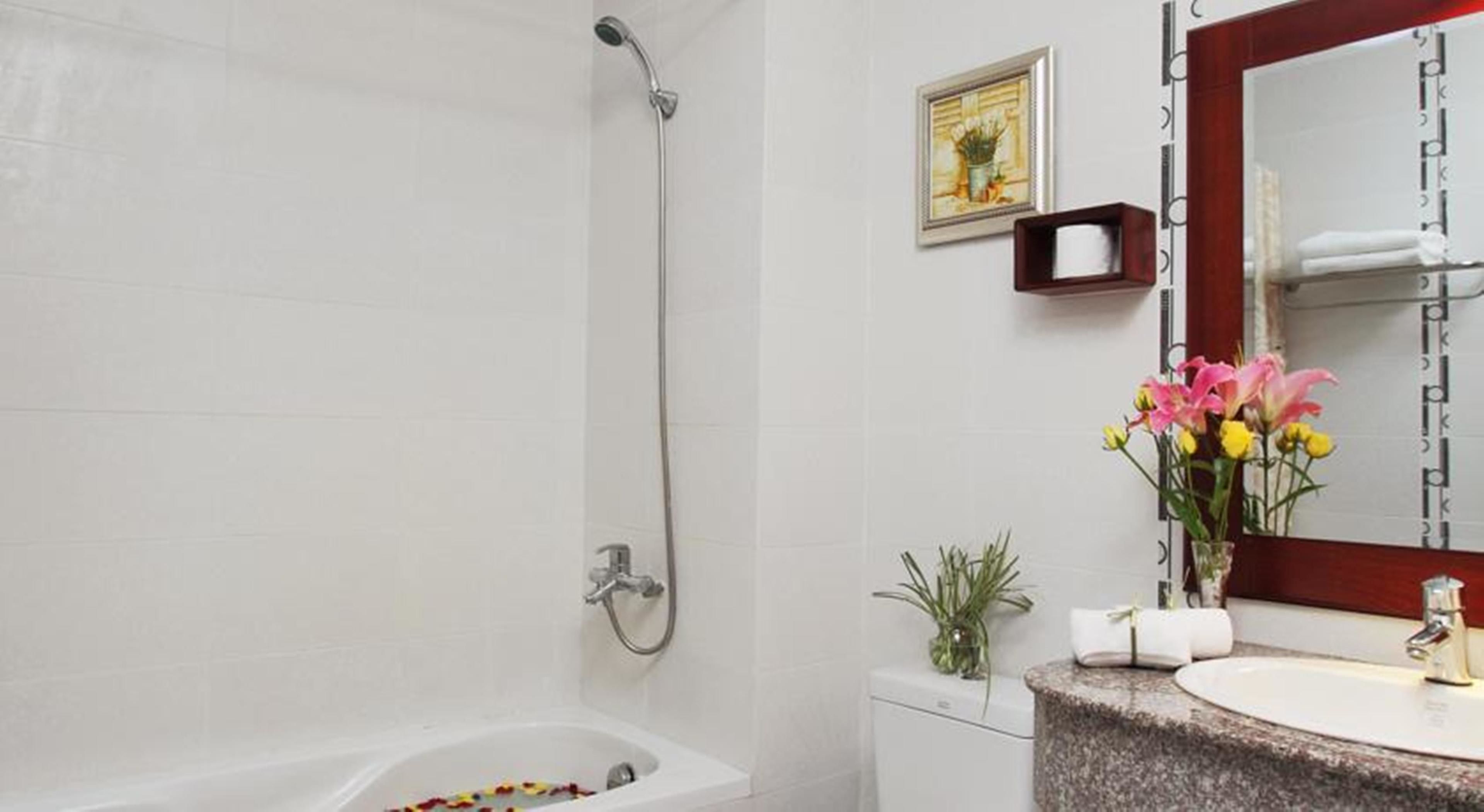 A bathroom with a bathtub, a shower, a sink with a mirror, and a vase with flowers.