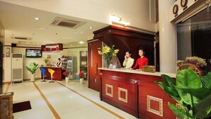 A hotel reception area with a wooden reception desk, two receptionists, a TV screen, and a reception sign. - Kim Yen Hotel (Ho Chi Minh City)