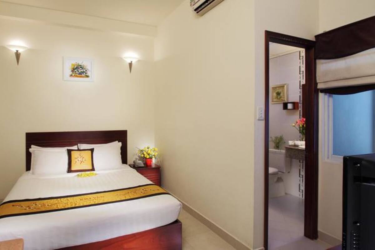 Ein Hotelzimmer mit einem Bett, einem Nachttisch und einem kleinen Schreibtisch mit Stuhl. Ein Badezimmer ist durch eine geöffnete Tür erkennbar.
