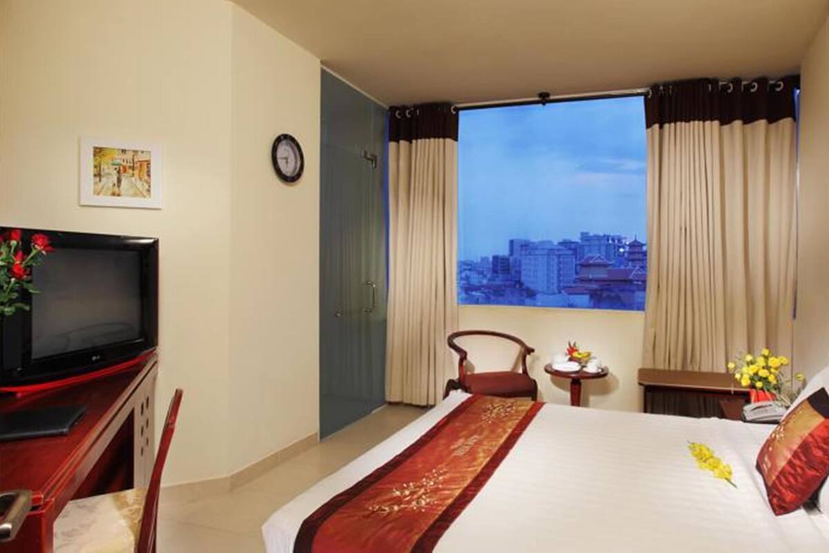 Ein Hotelzimmer mit Bett, Fernseher, Sessel, kleinem Tisch und einem Fenster mit Vorhängen.