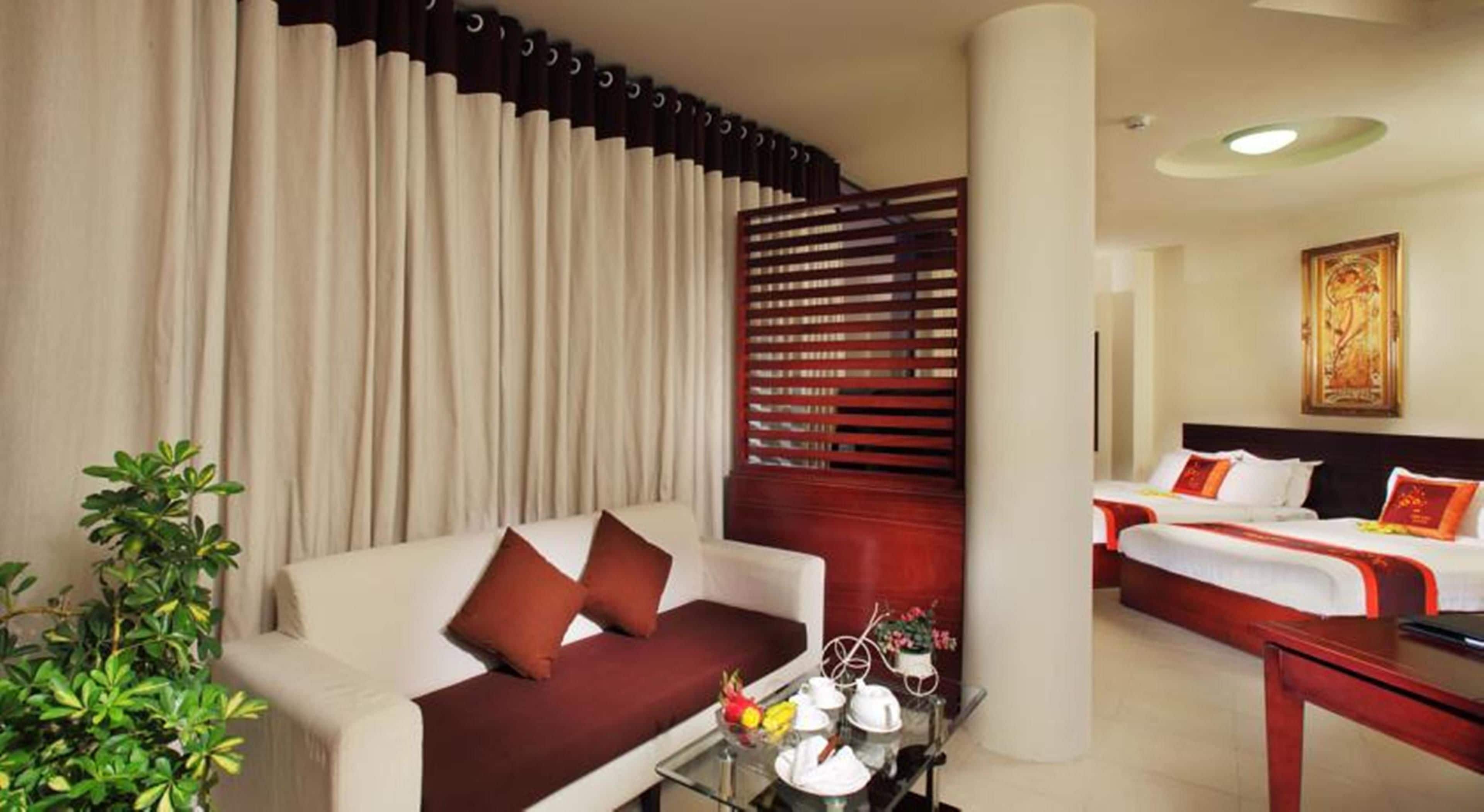 A hotel room with a bed, a sofa, a coffee table with a vase of flowers, and a plant.