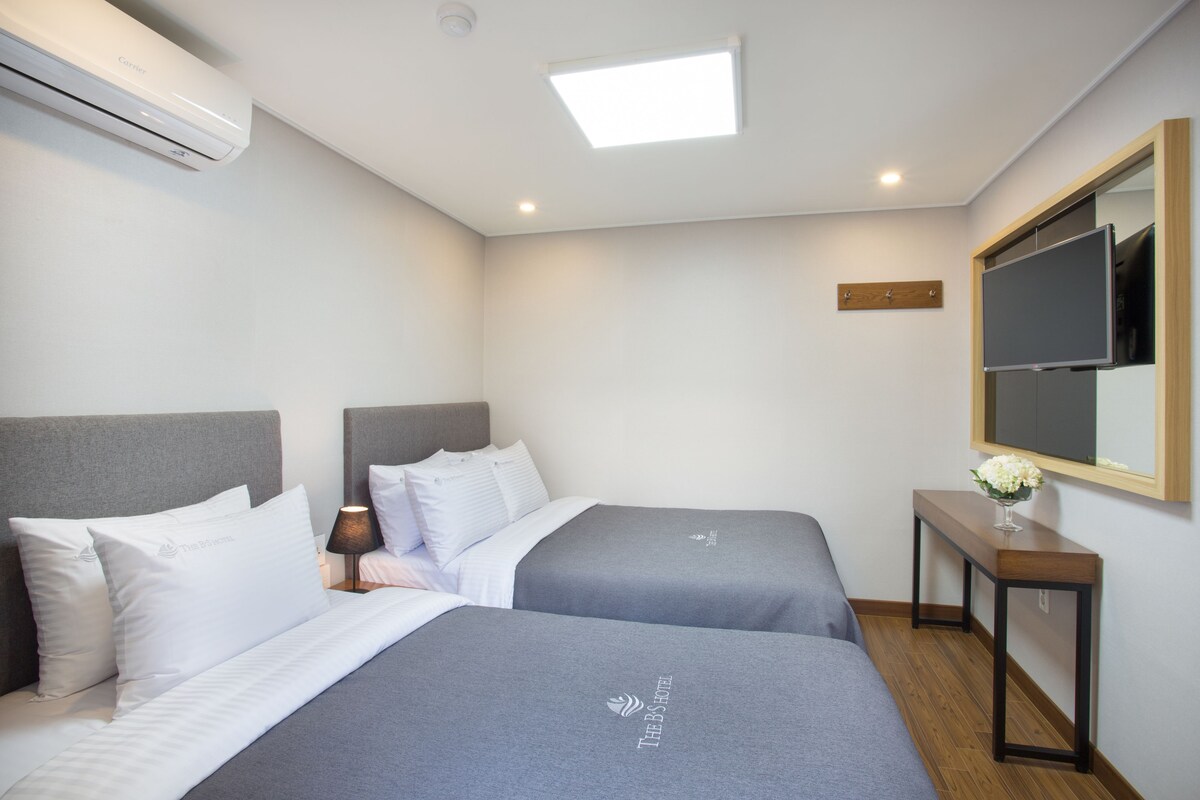 Une chambre d’hôtel avec deux lits, une table de chevet avec une lampe, un miroir et un appareil de climatisation.