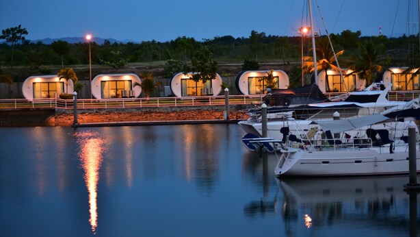 Un port de plaisance où sont amarrés plusieurs hébergements en forme de yacht, le long de l’eau, dotés de grandes fenêtres et d’espaces extérieurs aménagés pour se détendre.