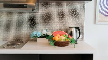 A kitchen with a tiled backsplash, a stainless steel kettle, and a fruit basket on the counter.