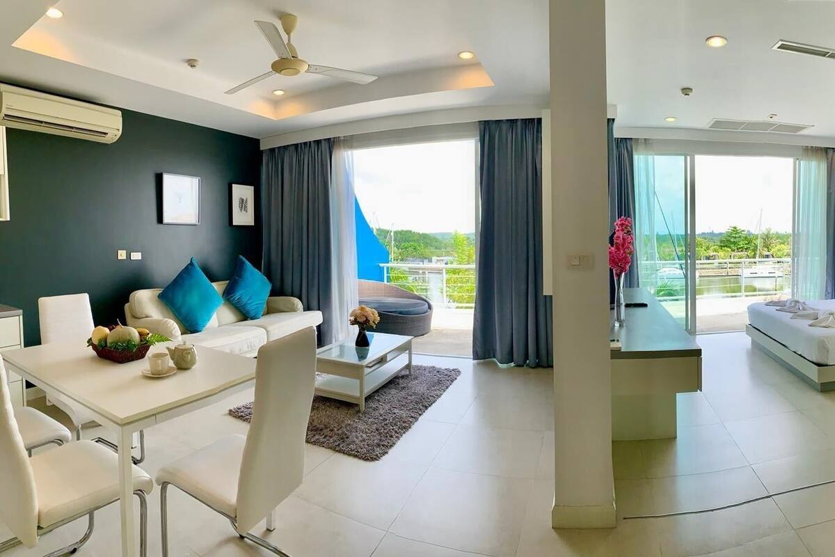 A modern hotel room with a dining area, a sofa, a bed, and a balcony with a view.