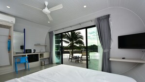 Une chambre d’hôtel moderne dotée d’un grand lit, d’un bureau avec une chaise, d’un téléviseur fixé au mur et d’un balcon offrant une vue sur les palmiers.
