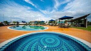 Une grande piscine extérieure avec un bord carrelé, entourée de chaises longues et de parasols, sous un ciel dégagé.