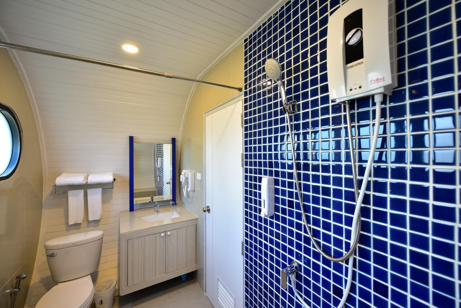 Un baño con inodoro, lavamanos, espejo, toallero y zona de ducha con azulejos azules.