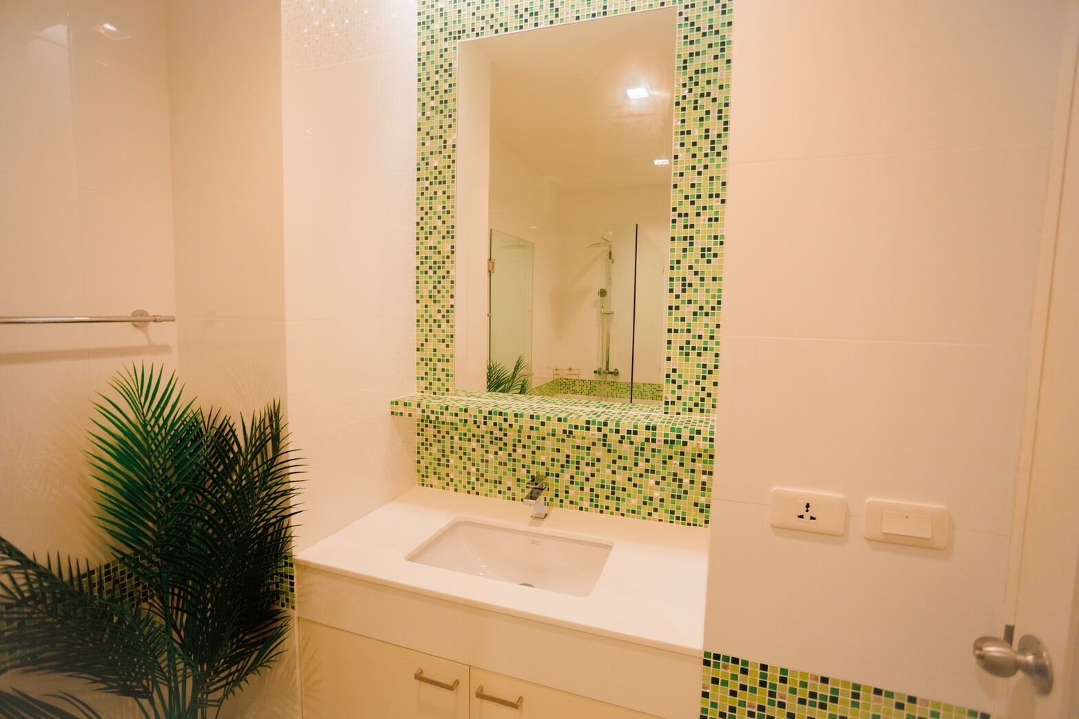 A bathroom with a sink, mirror, and green mosaic tiles.