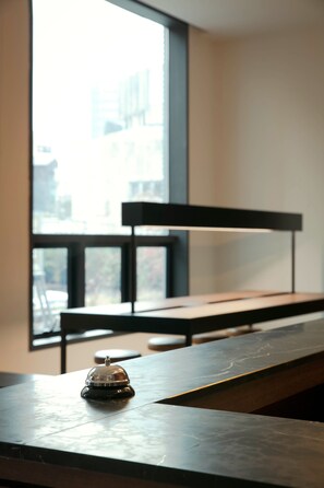 Une chambre d’hôtel moderne dotée d’une grande fenêtre, d’un bureau en bois et d’une petite table sur laquelle se trouve une cloche.