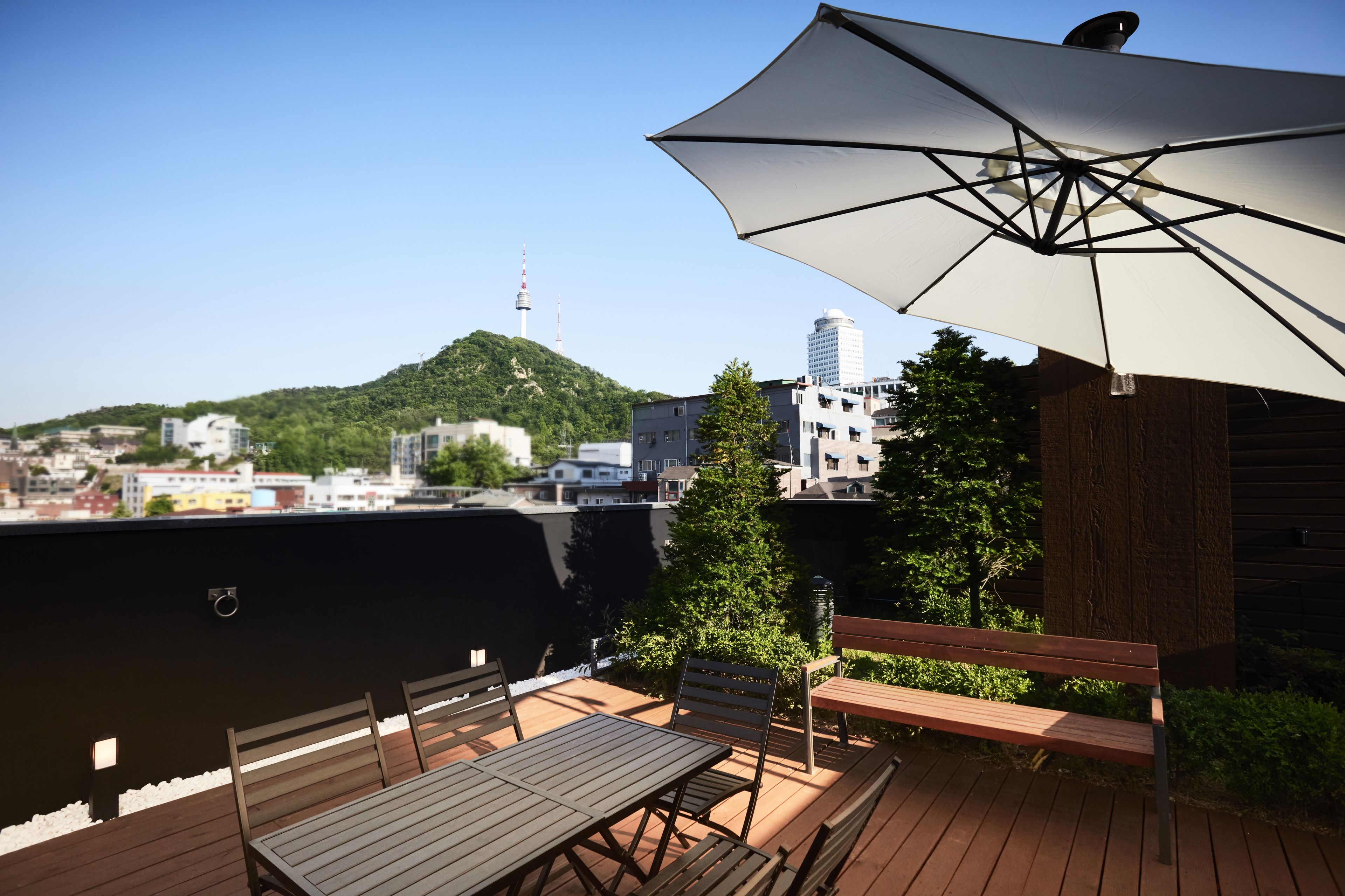 An outdoor patio with a table and chairs, a large umbrella, and a view of a cityscape with a hill and a tower in the distance.