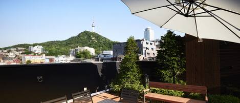 An outdoor patio with a table and chairs, a large umbrella, and a view of a cityscape with a hill and a tower in the distance.