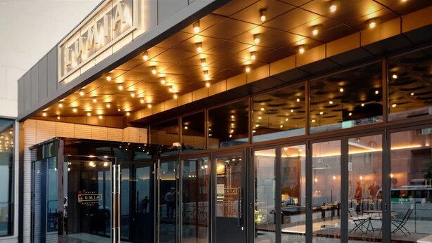 Ein moderner Hotelzugang mit Glastüren, einer Beschilderung über der Eingangstür und einem gut beleuchteten Innenraum, der durch die Glasfläche sichtbar ist.