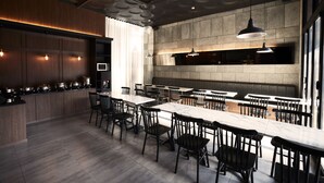 Ein modernes Restaurant mit einer langen Theke, mehreren Tischen und Stühlen. Es gibt eine Küchenzeile mit einer Steinwand und hängenden Lampen.