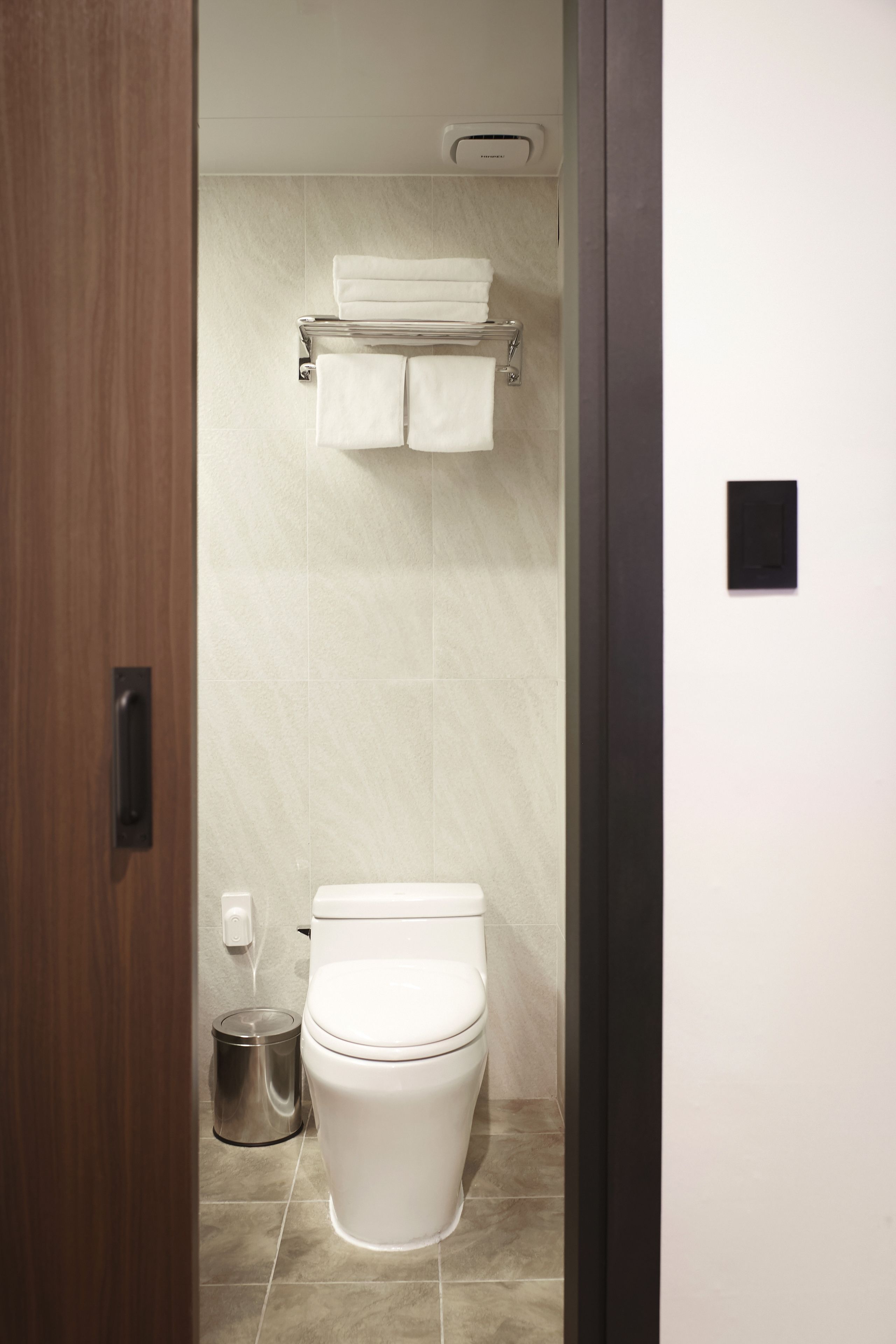 Un baño moderno con inodoro, un bote de basura y un perchero con dos toallas.