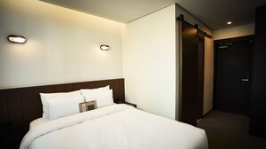 Ein Hotelzimmer mit einem ordentlich bezogenen Bett, einem Holz-Kopfteil und zwei Wandleuchten.