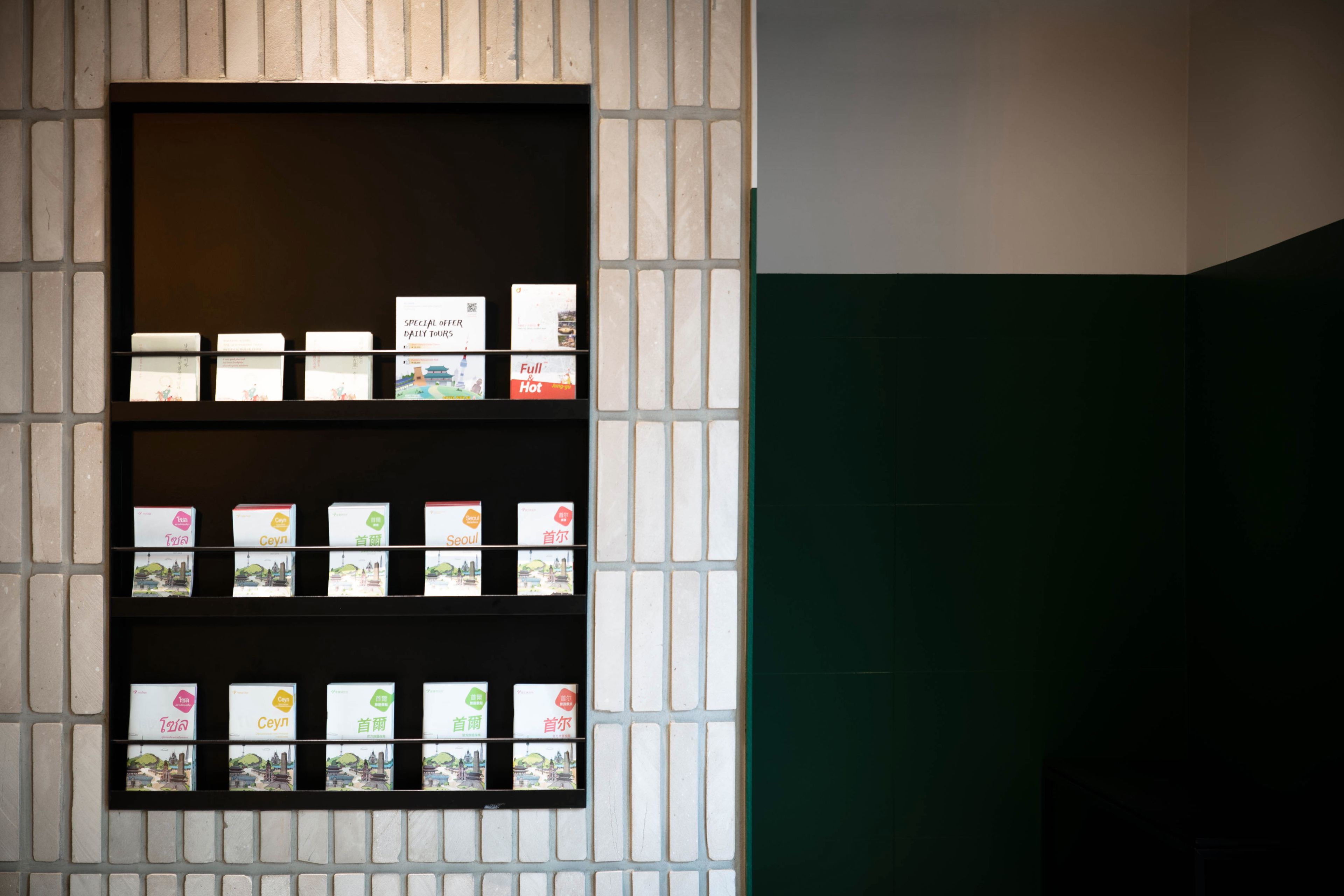 Una exhibición de postales con diversos diseños y textos, dispuestas en estanterías frente a una pared de ladrillo.