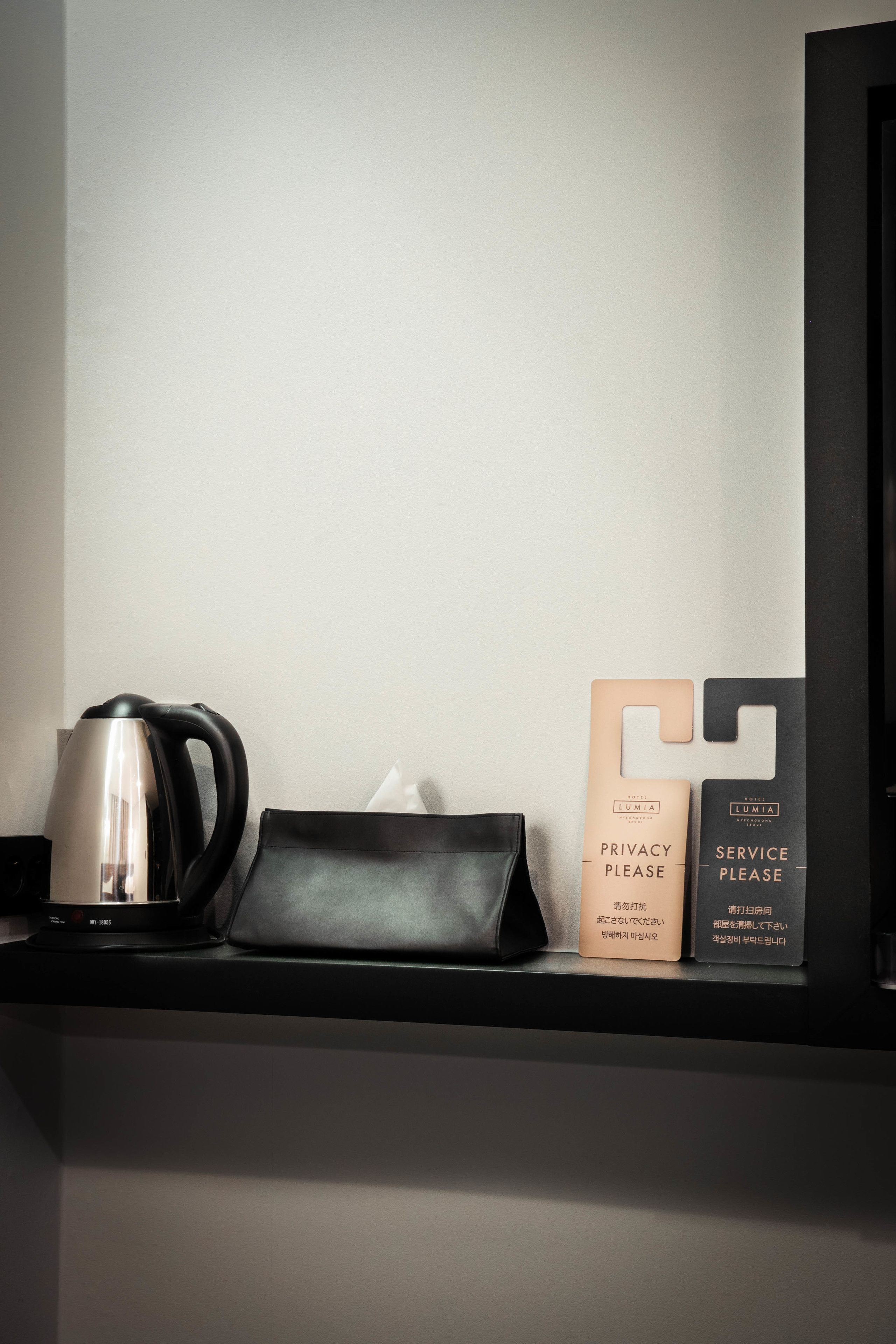 A black tray with a stainless steel kettle, a tissue box, and two service request cards on a shelf.