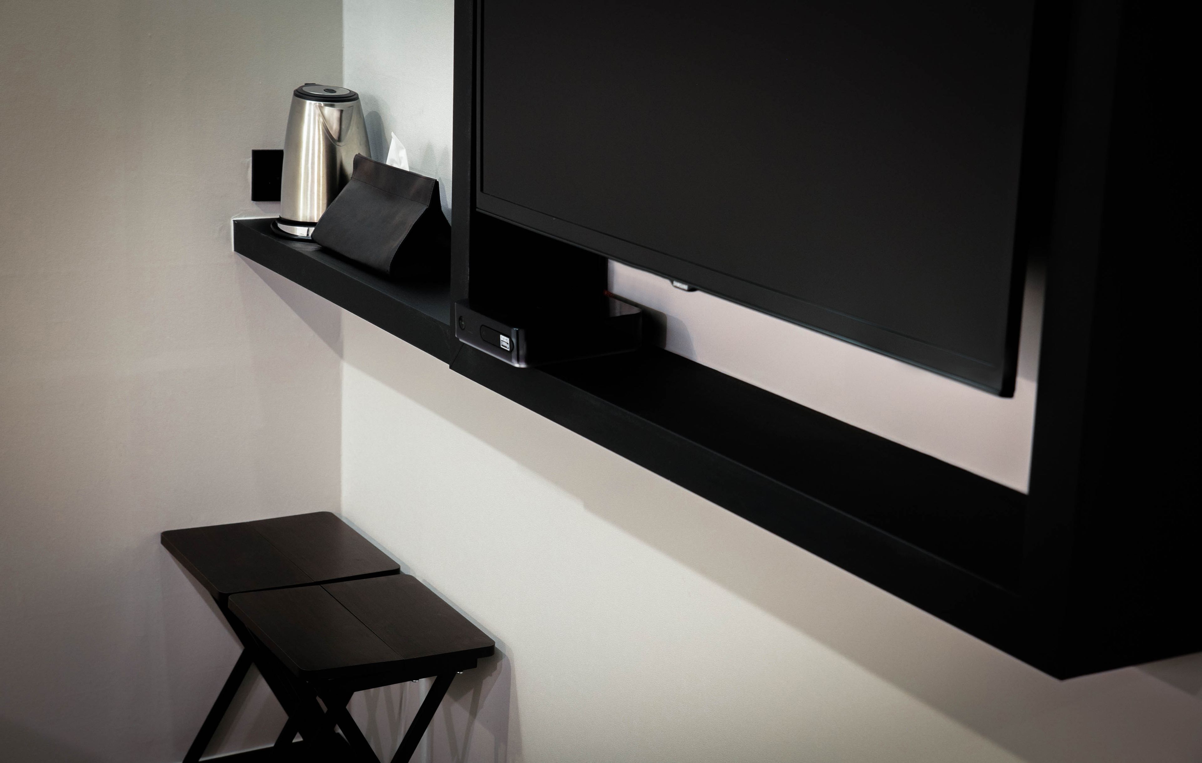 A modern room with a flat-screen TV mounted on a black shelf, a small black table, and a stainless steel kettle.